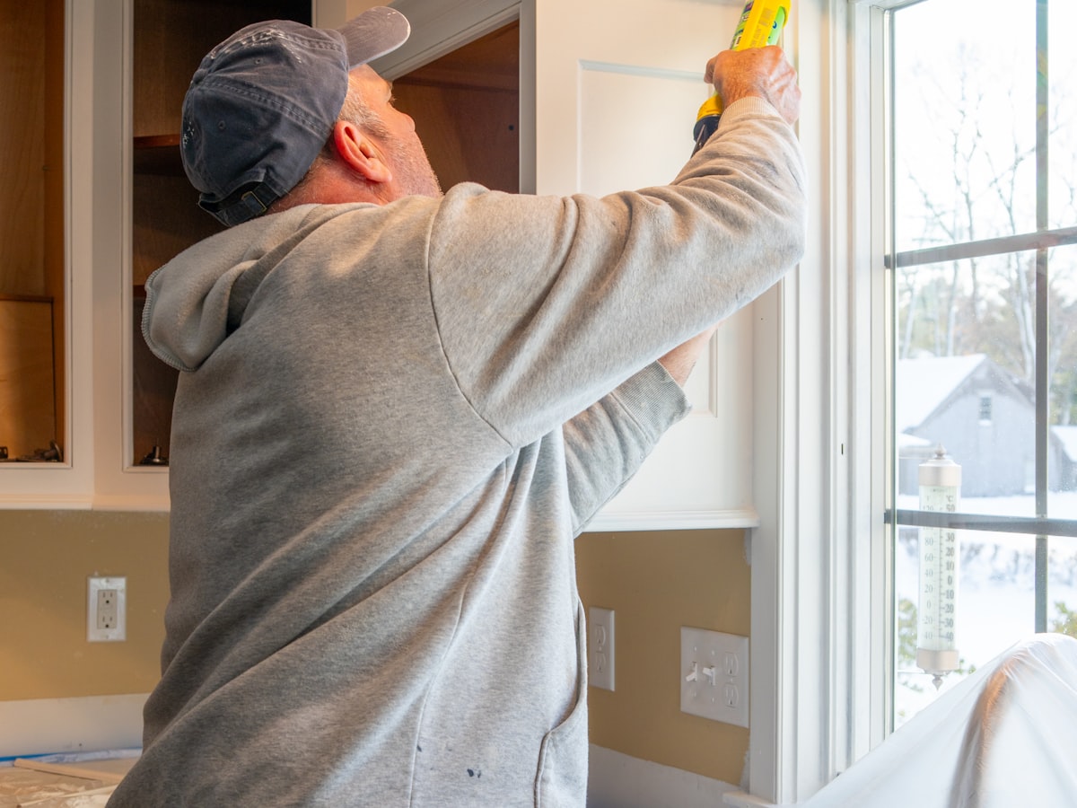 A handyman sealing a window frame indoors