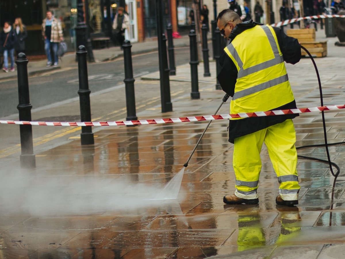 A worker pressure washing a paved surface